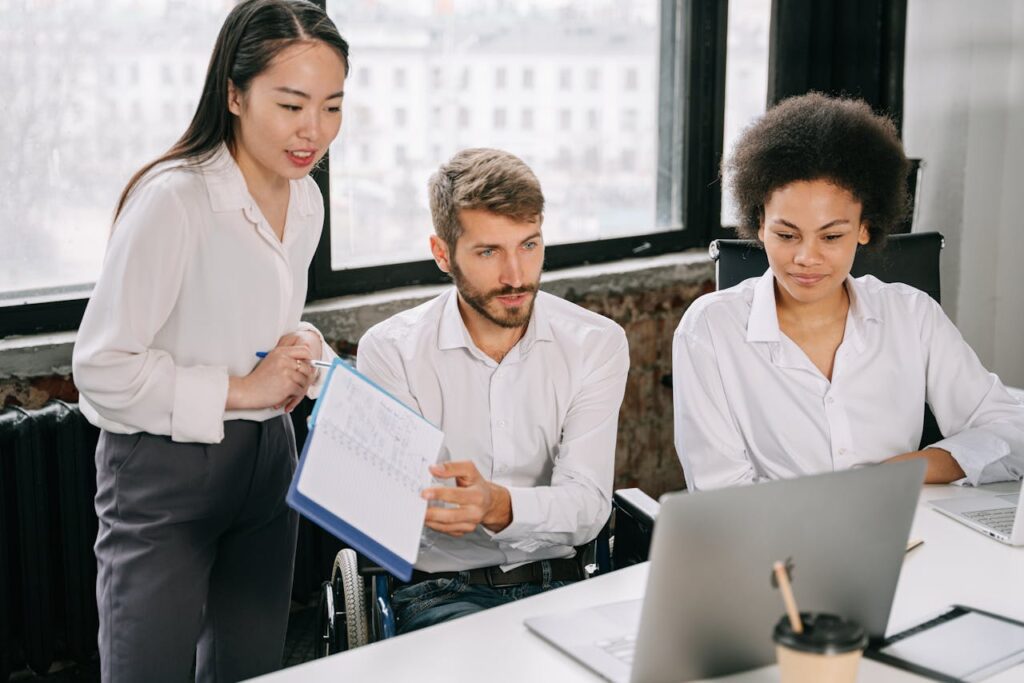 Three people in business attire discussing while looking at a laptop screen