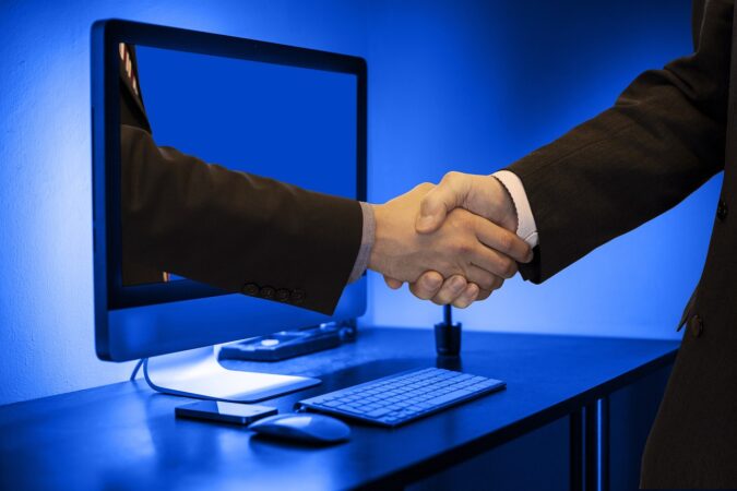 Handshake with one of the hands framed as coming from a computer monitor